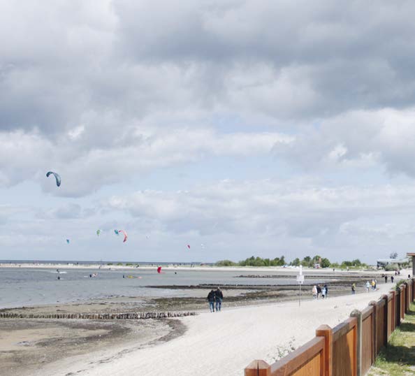 Blick auf das Meer mit Gleitschirmfliegern und Spaziergängern am Strand 