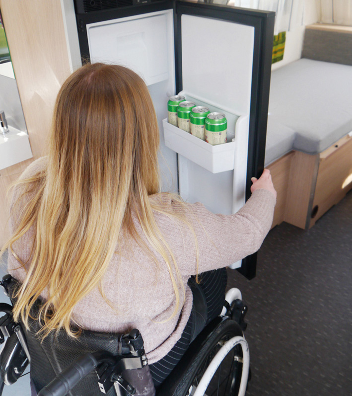 Frau im Rollstuhl öffnet einen Kühlschrank 
