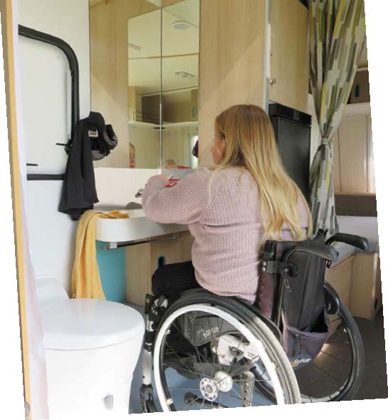 Frau im Rollstuhl sitzt vor einem Waschbecken mit Spiegel 