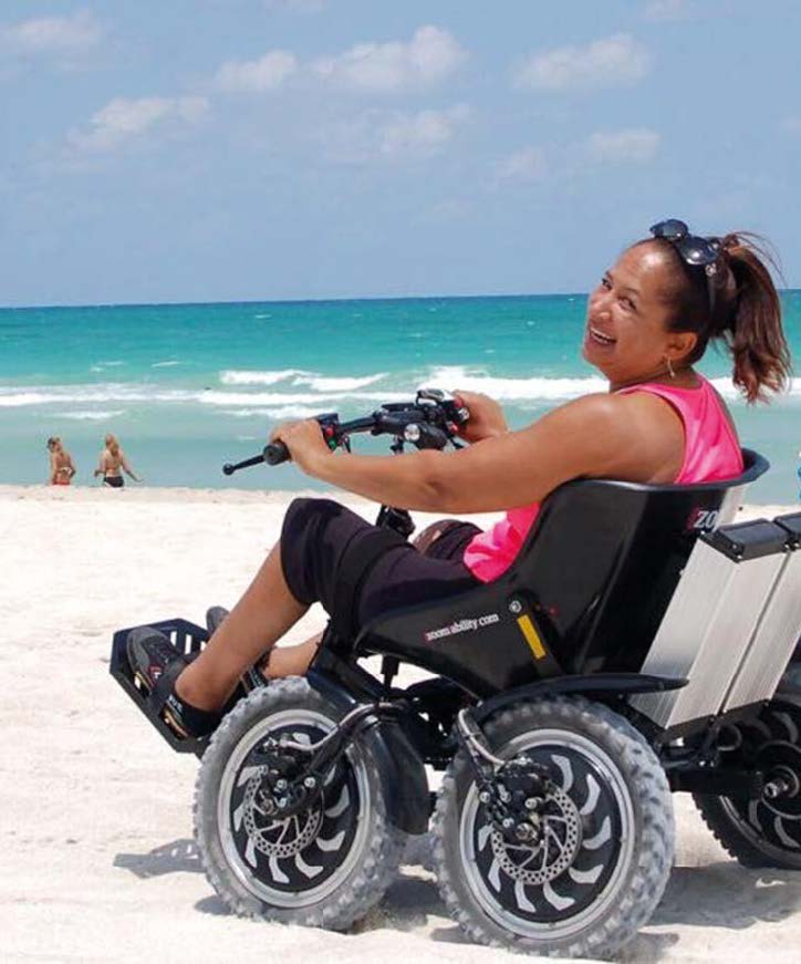 Elektrischer Geländerollstuhl  mit großen Rädern mt Fahrerin am Strand
