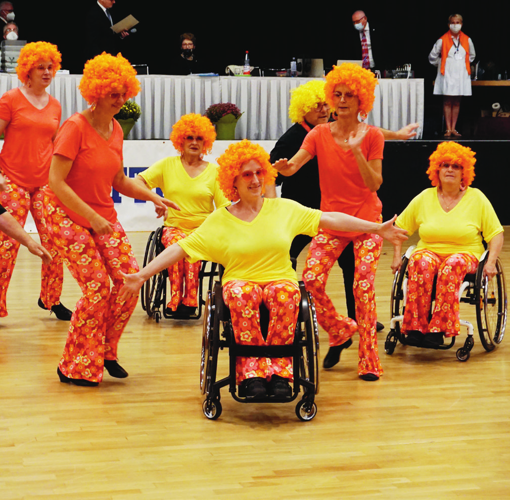 Mehrere Personen mit Rollsuhl und Perrücken beim üben eine Tanzfigur ein