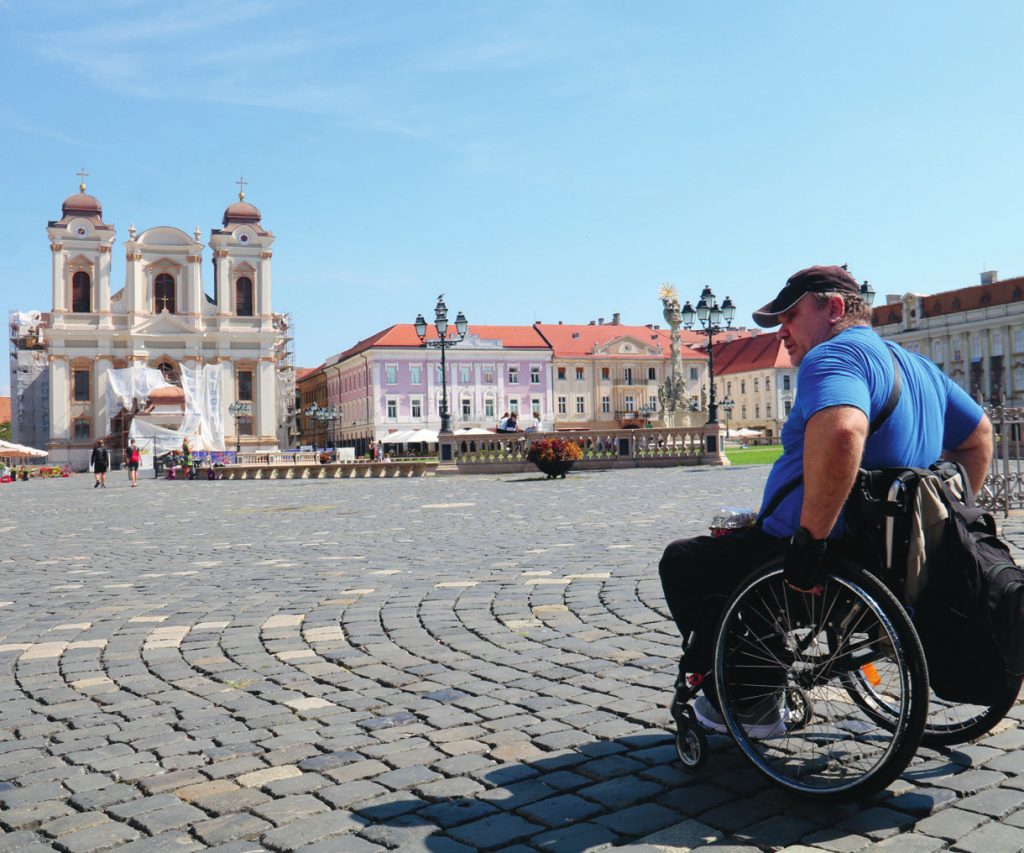 Mann im Rollstuhl steht auf Kopfsteinpflaster