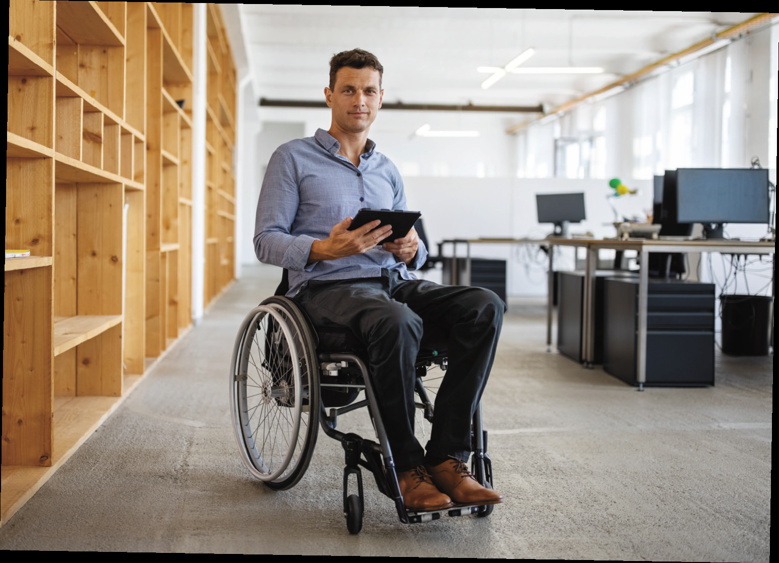 Mann im Rollstuhl steht im Büro und schaut auf ein Smartphone